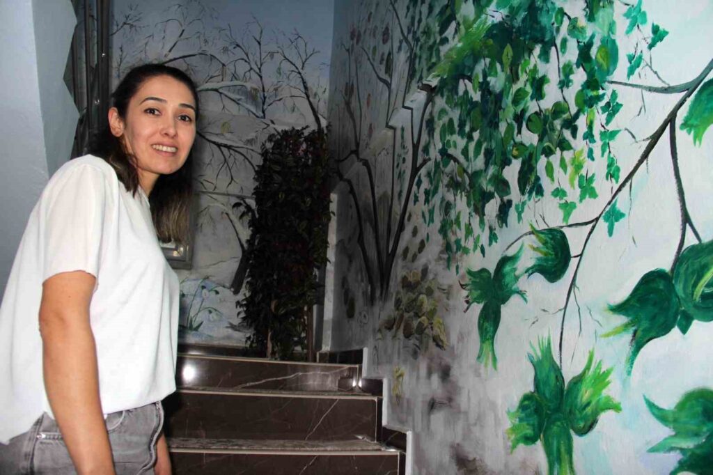 Giresun’un Piraziz ilçesinde fındık kırma atölyesi işleten Demet Öztürk, sanatı ve tarımı aynı çatı altında buluşturdu. Evinin merdiven duvarlarını yağlı boya resimlerle donatarak fındığın on iki aylık gelişim sürecini anlatan Öztürk, hem sanata hem de geleneksel tarıma dikkat çeken özgün bir projeye imza attı.

Bir dönem fındık atölyesini evinin üst katında işleten Öztürk, merdivenleri çıkan misafirlerin ilgisini çekmek ve fındığın doğadaki döngüsünü anlatmak için ilginç bir fikir geliştirdi. Görsel Sanatlar Öğretmeni Mustafa Seyis’in desteğiyle başlayan bu imece çalışması, yaklaşık iki ayda tamamlandı.

“Bu Duvarlar Fındığa Olan Saygımızın İfadesi”
Demet Öztürk, her sabah işe giderken bu renkli duvarlardan geçtiğini belirterek, "Her ayın fındıkla ilgili ayrı bir anlamı var. Bu duvar sadece bir süs değil, fındığa duyduğumuz saygının da bir ifadesi" dedi.

Sadece fındık değil, Karadeniz’in doğal zenginlikleri de resimlerde yer aldı. Bahçede yetişen sakarca, çuha, menekşe ve mimoza gibi çiçekler; ayrıca fındık bahçelerinde zararlılarla beslenen ve bolluk bereketin simgesi olan kara tavuk da fındık dallarına yuva yapmış haliyle tasvir edildi.

Ziyaretçilerin Uğrak Noktası Oldu
Fındığın 12 ay boyunca geçirdiği evrelerin sanatsal bir dille anlatıldığı merdiven duvarları, artık bir ziyaret alanına da dönüşmüş durumda. Sanata ilgi duyanların yanı sıra tarımsal süreçlerle ilgili bilgi edinmek isteyen birçok kişi, bu özel çalışmayı görmek için Öztürk’ün evini ziyaret ediyor.

Türkiye’de İlk: Fındığın Ay Ay Görselleştirilmesi
Demet Öztürk, Türkiye’de fındığın tüm yıl süren gelişim sürecini anlatan benzer bir çalışma olmadığını vurgularken, bu girişimin hem kültürel hem de eğitici bir değer taşıdığını söyledi. “Bu çalışma, doğaya duyduğumuz saygıyı sanat yoluyla ifade etmenin bir örneği oldu” dedi.

